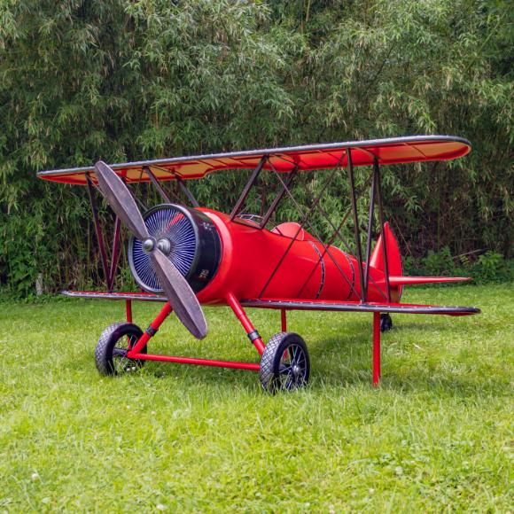 Red biplane model on grass with green foliage in the background